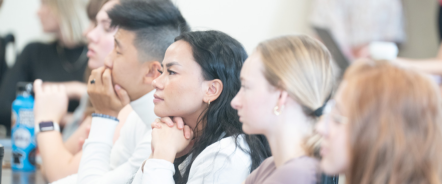 Multiple students listen attentively from a shared desk in a classroom.