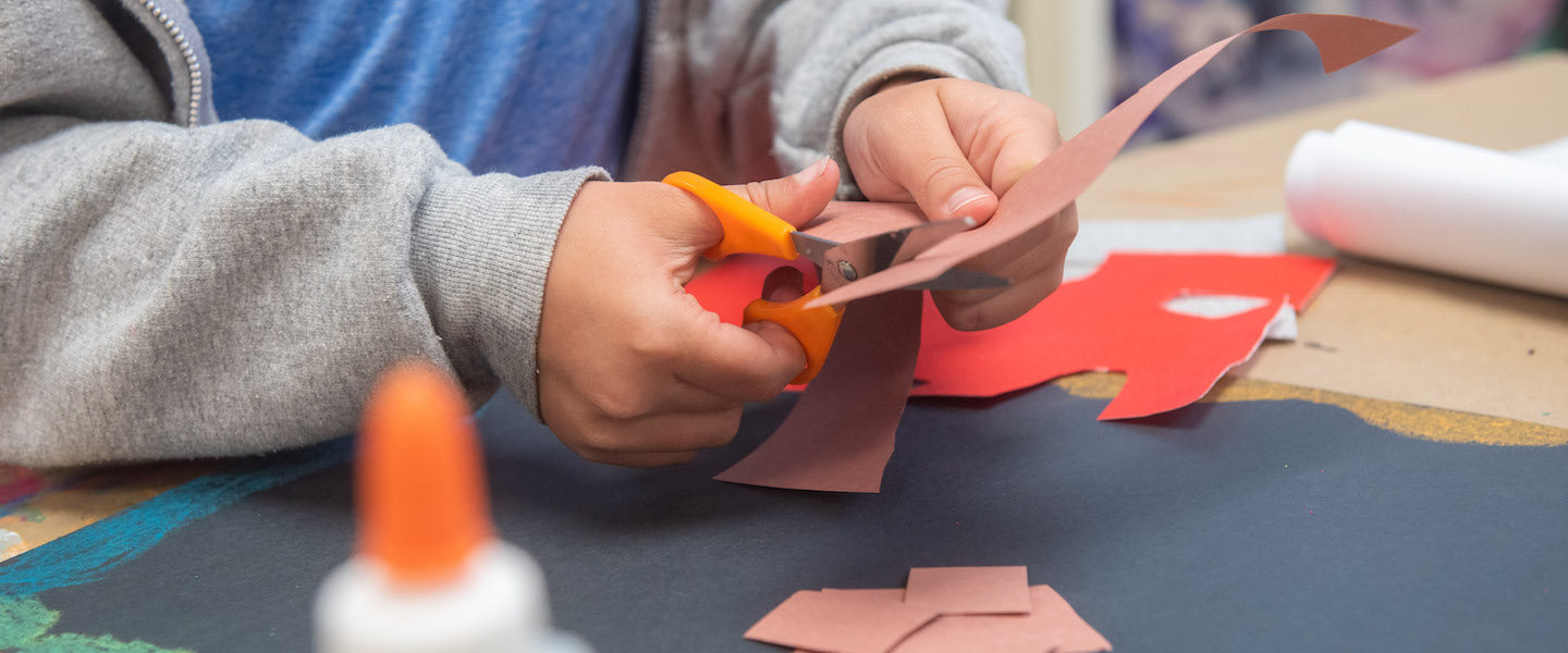 Young student cutting construction paper with scissors