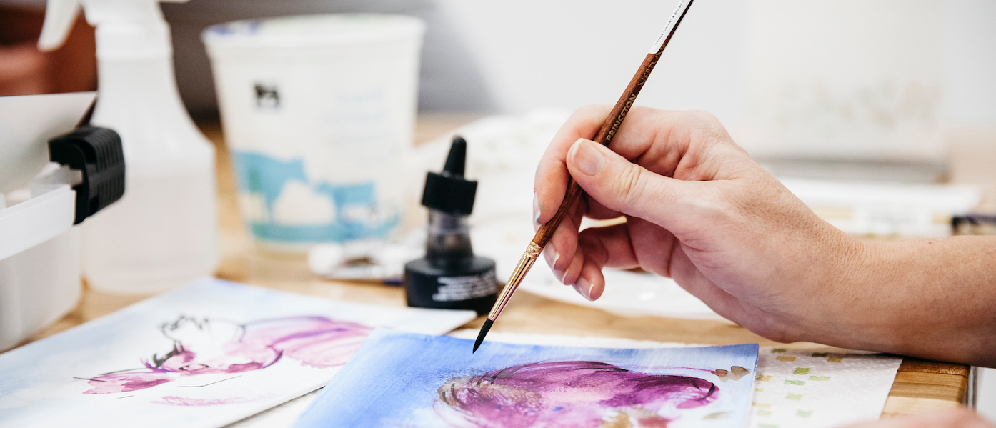 Close up of person painting on paper with blues and purples