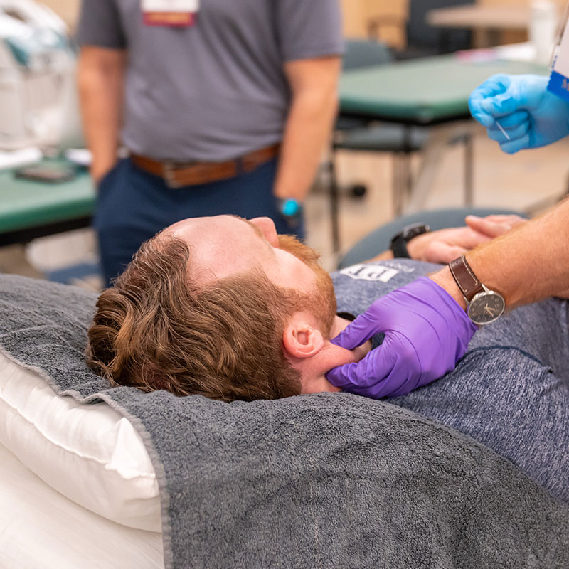 A physical therapist working with a patient's neck while they lay on a table