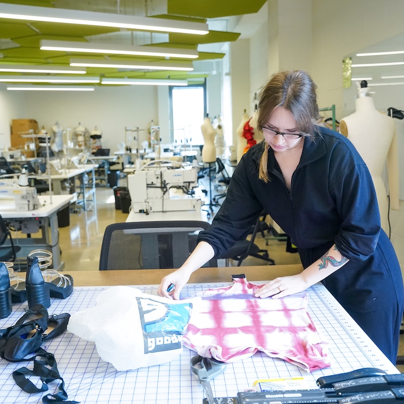 Fashion design student measuring fabric on a sewing table in O'more desing class room