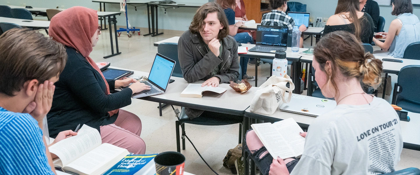 Students writing on laptops and paper in a classroom