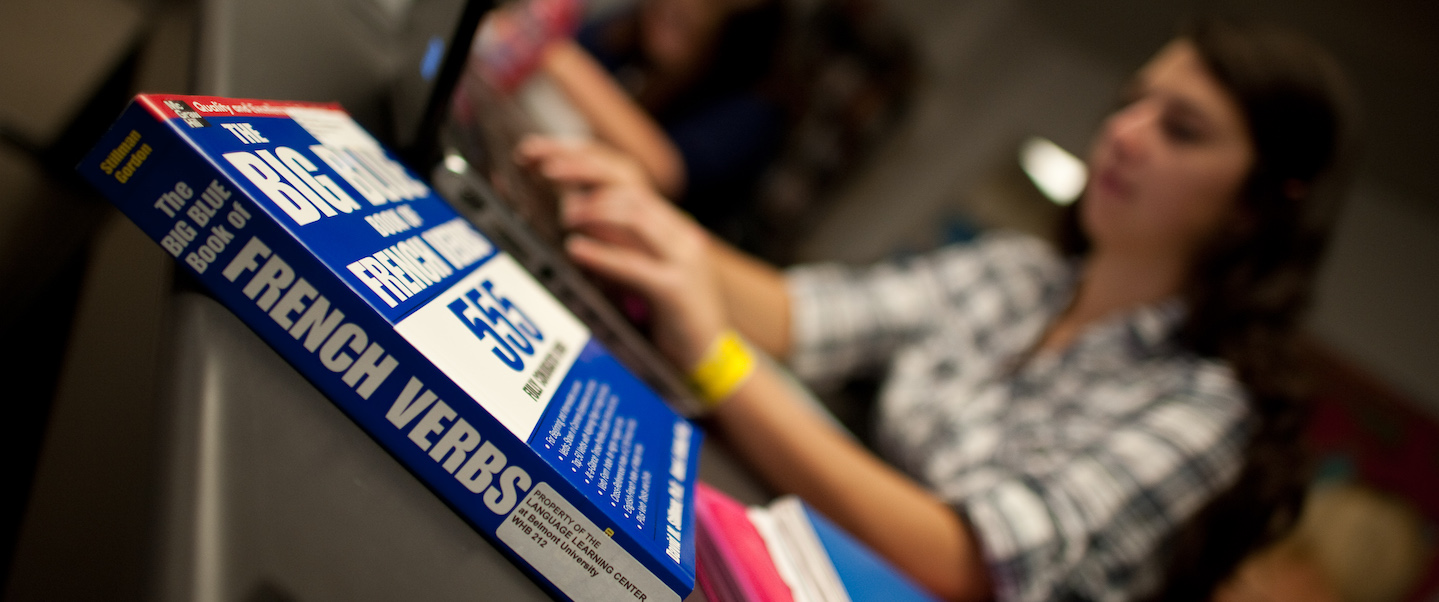 Student sitting studying beside a book for French Verbs