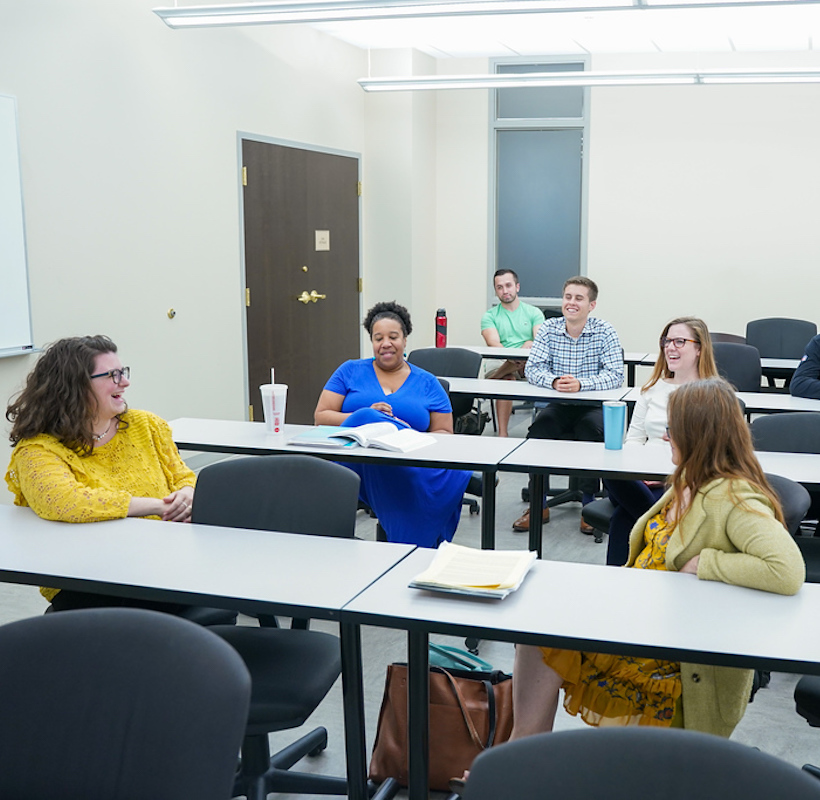 6 students sitting in a classroom, laughing and having a discussion