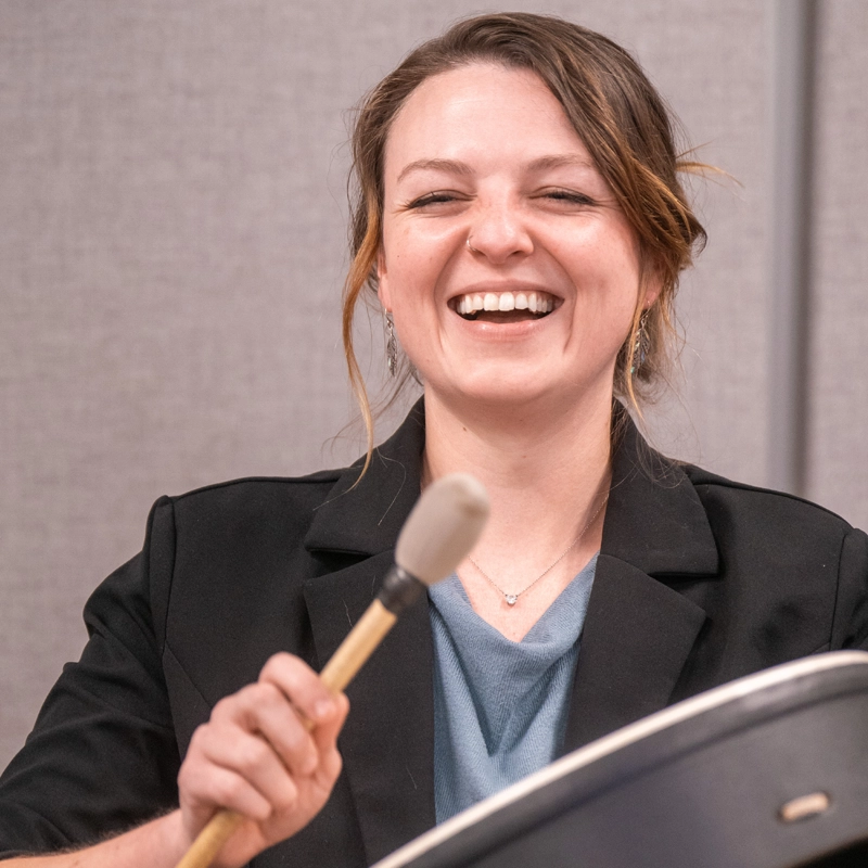 A female student playing a drum and laughing.