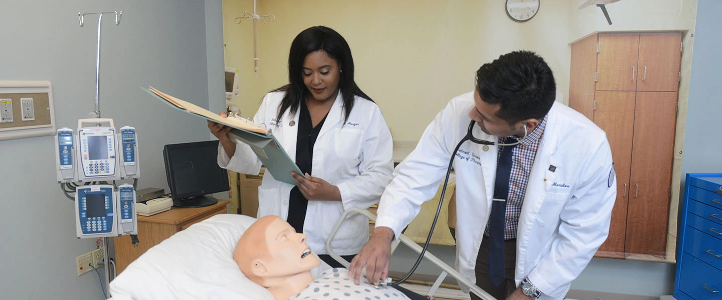 Two pharmacy students working with a human simulator during a lab exercise