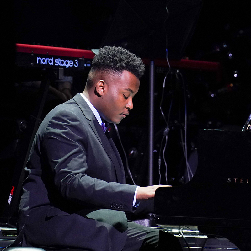 A male student sits at a grand piano and plays.