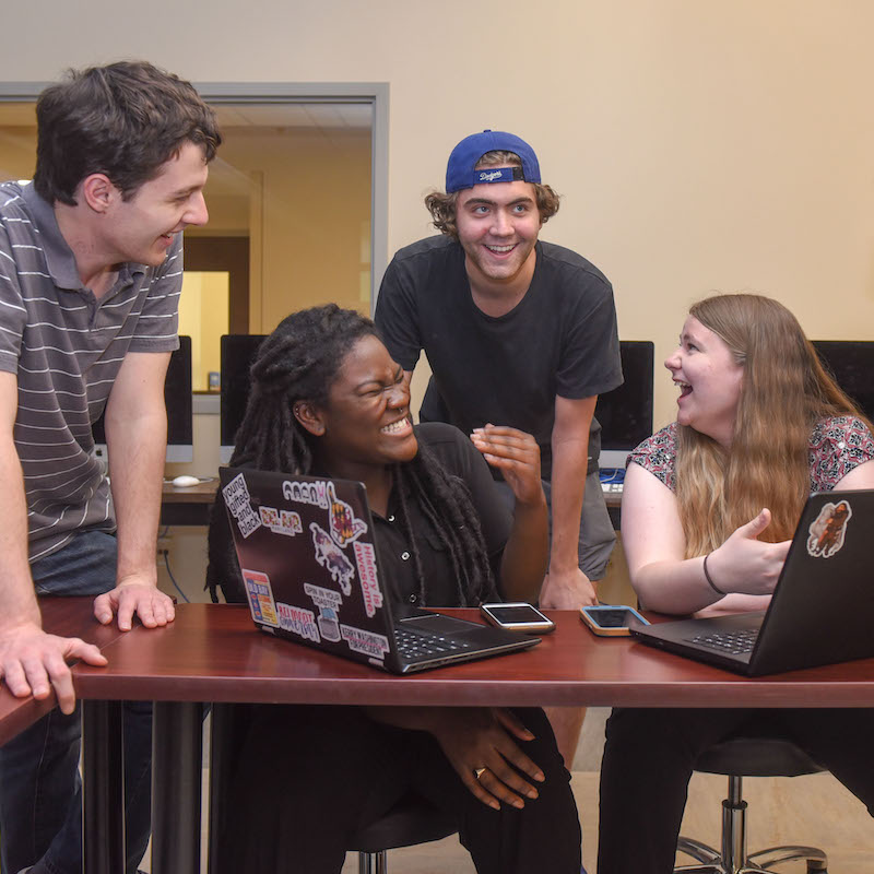 students having small group discussion in class room in front of a laptop