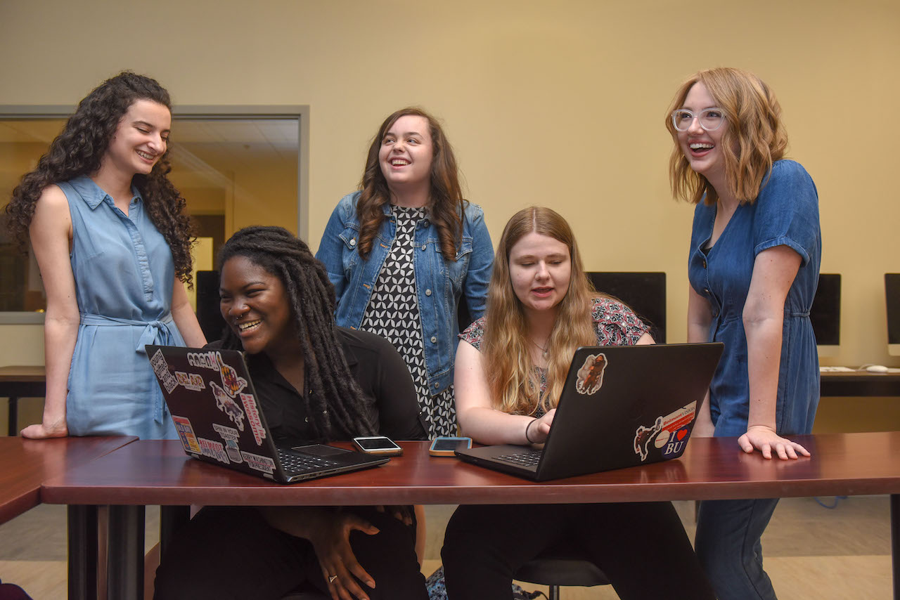 Students standing around laptops studying social media management