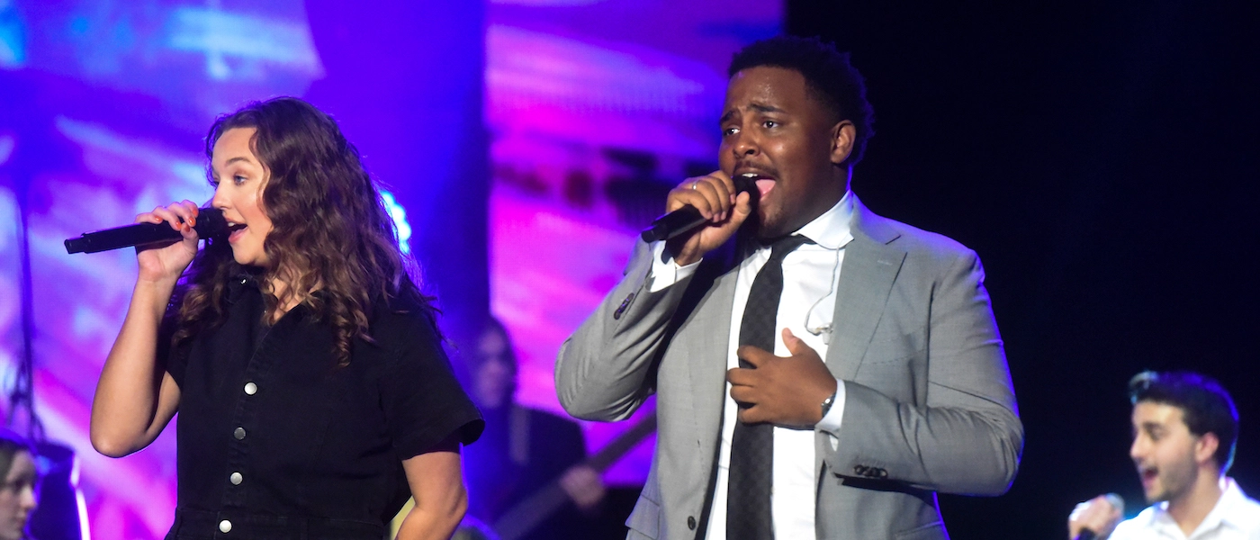 two students, one male and one female, performing onstage in front of a blue and purple backdrop.