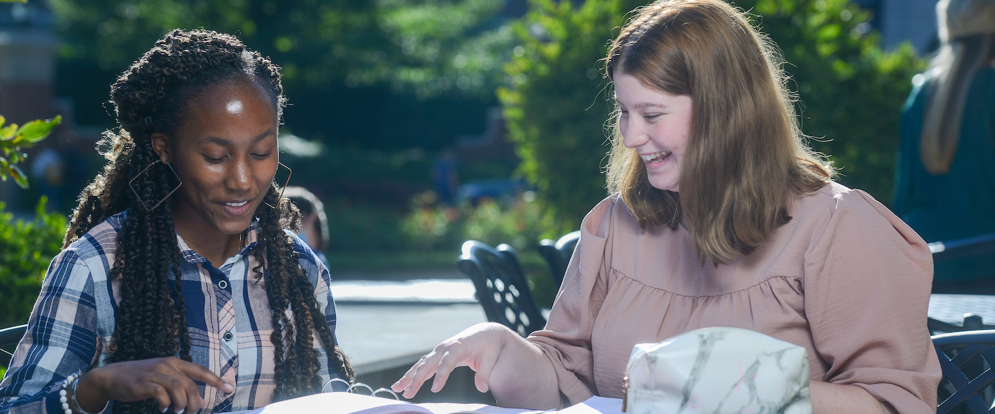 Two students chat at an outdoor table