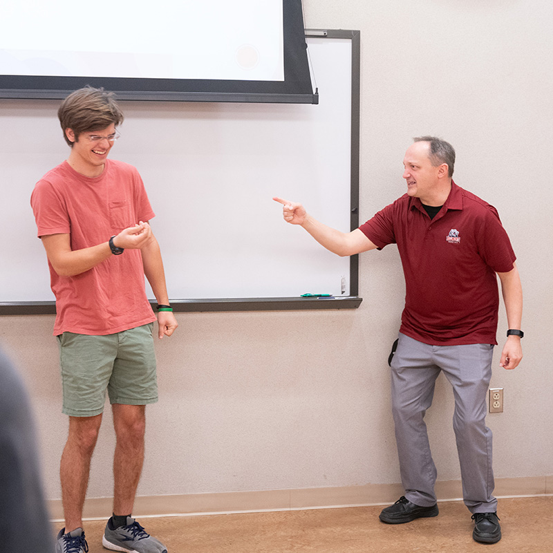 A student and a professor play a theater game and stand laughing together.