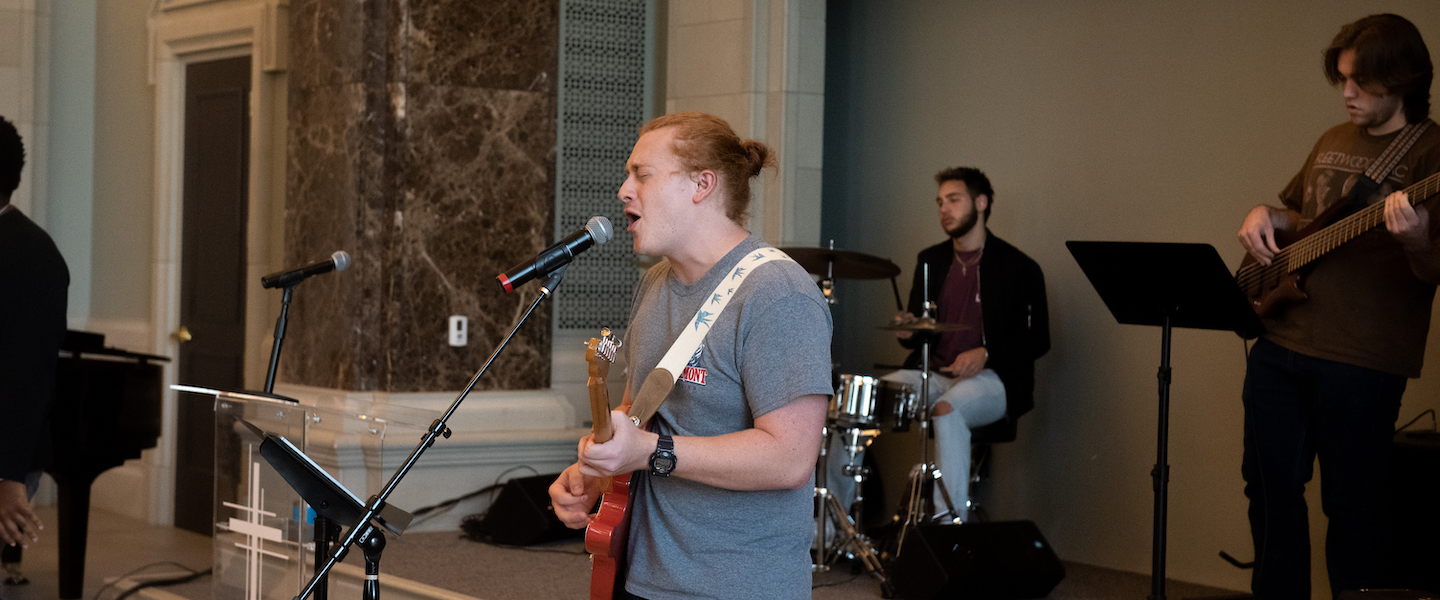 Student singing and playing guitar with band during chapel