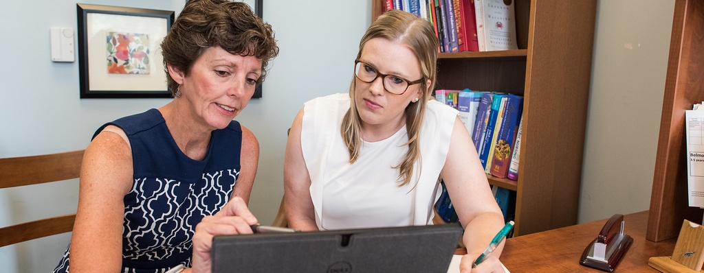 A faculty member is advising a student while both are seated at a table and looking at a monitor