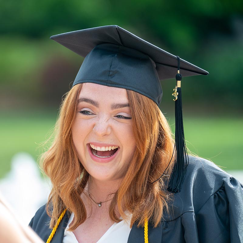 Graduate smiling at person taking their picture on their graduation day