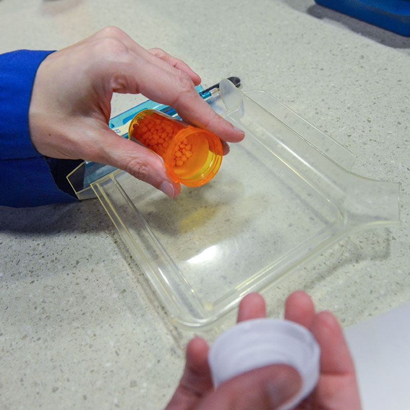 A close of a pharmacists hands counting pills with a pill counter 