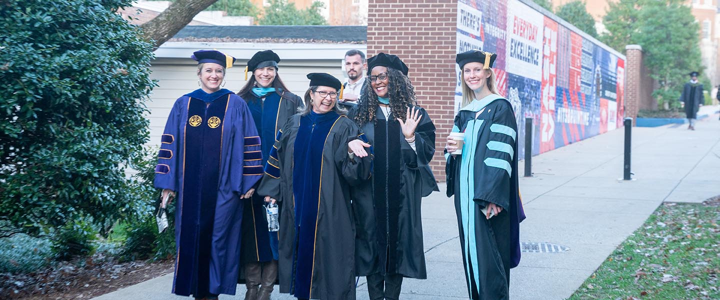 Faculty members smile for the camera while wearing their doctorate caps and gowns before graduation ceremony