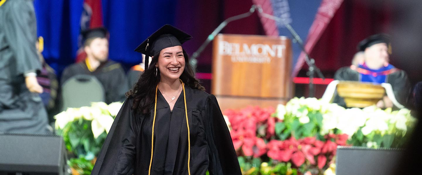 Student smiles in cap and gown during graduation ceremony after receiving diploma