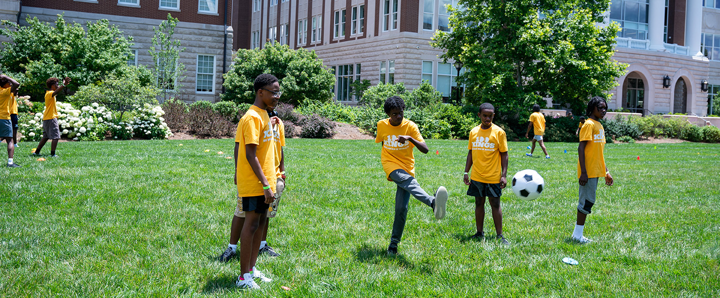 Young children playing soccer in yellow shirts on the Belmont lawn.