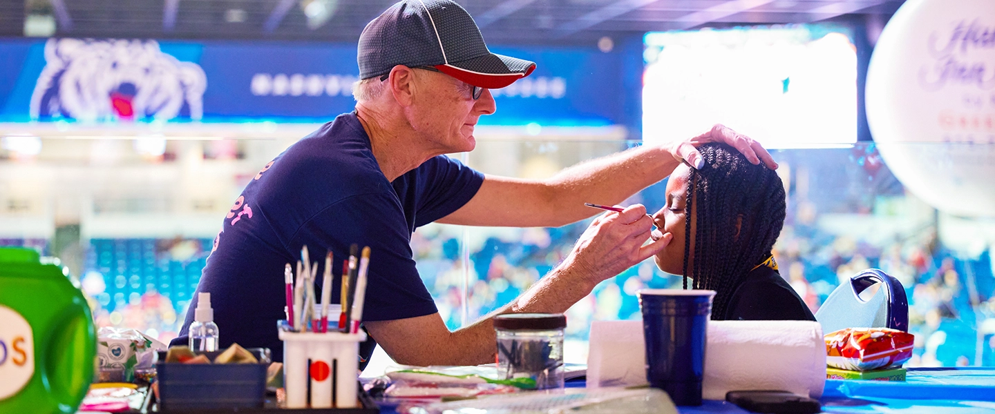 A coach painting a child's face for communtiy night in the basketball court.