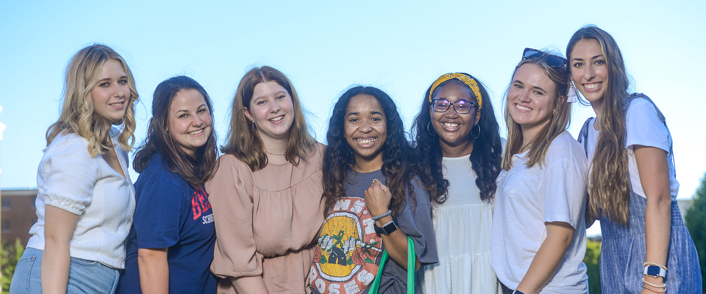 A group of female education students huddle together and smile at the camera.