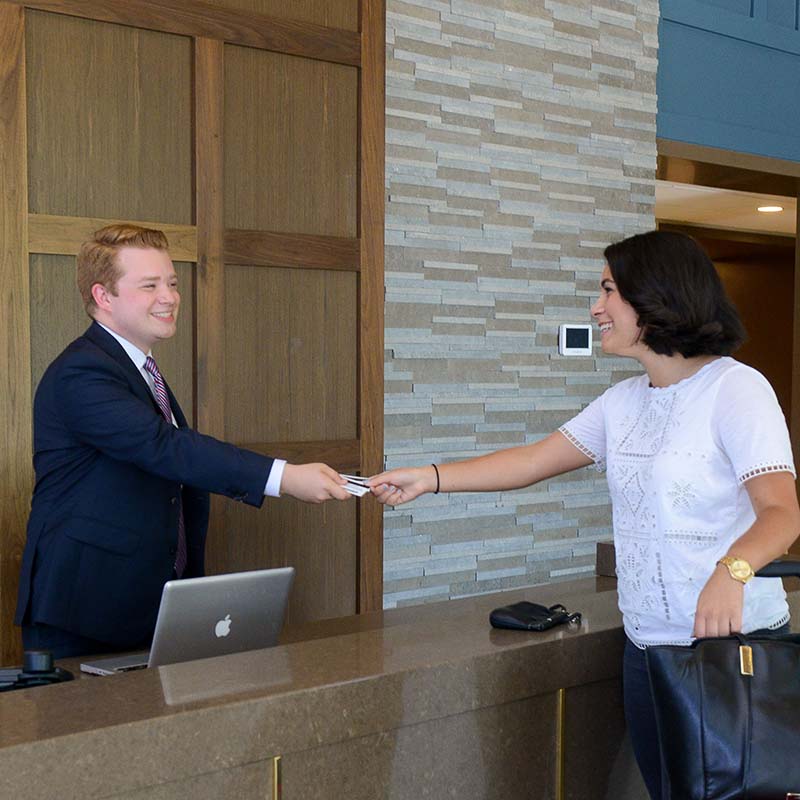 An indoor picture of a man in business suit handing a card over the front desk to a woman