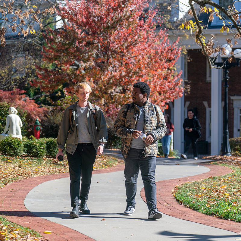 2 students talking and walking outside on the historic side of campus on a sunny fall day