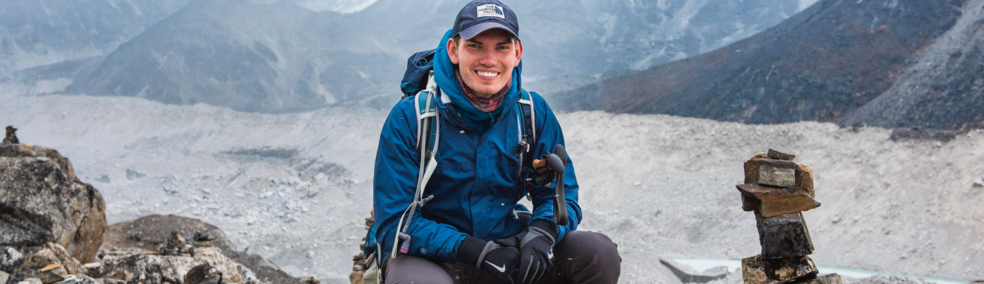 Lumos Traveler in a blue jacket posing with the Himalayan Mountains in the background