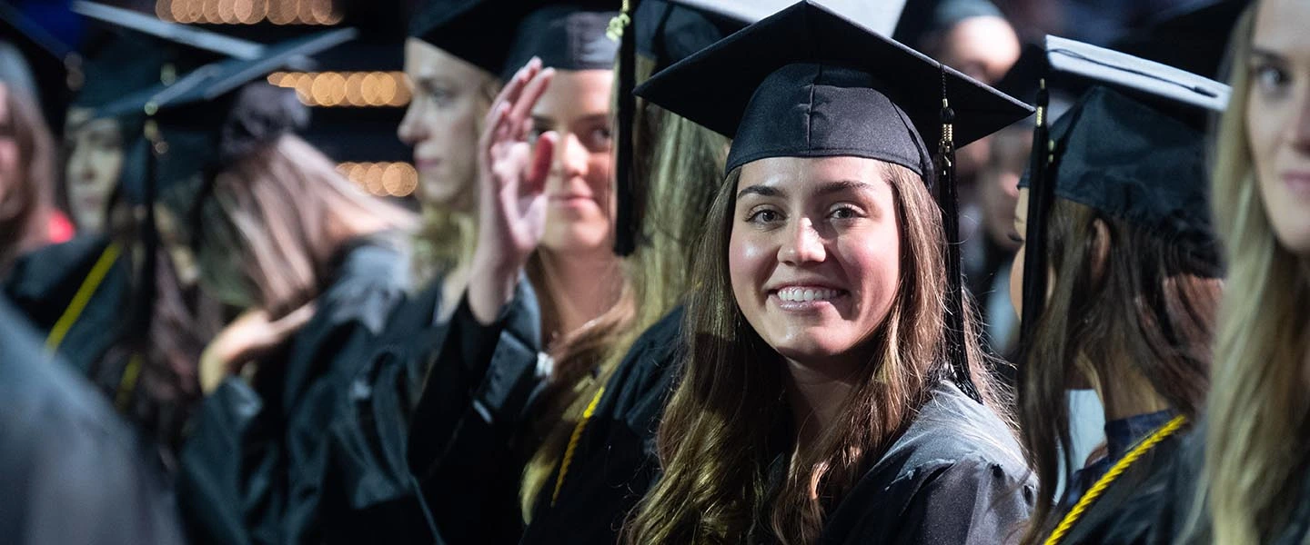 Student in at graduation in cap and gown smiling at camera