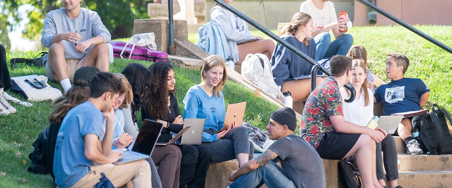 Students gathered outside on a staircase on the historic side of campus have a group discussion