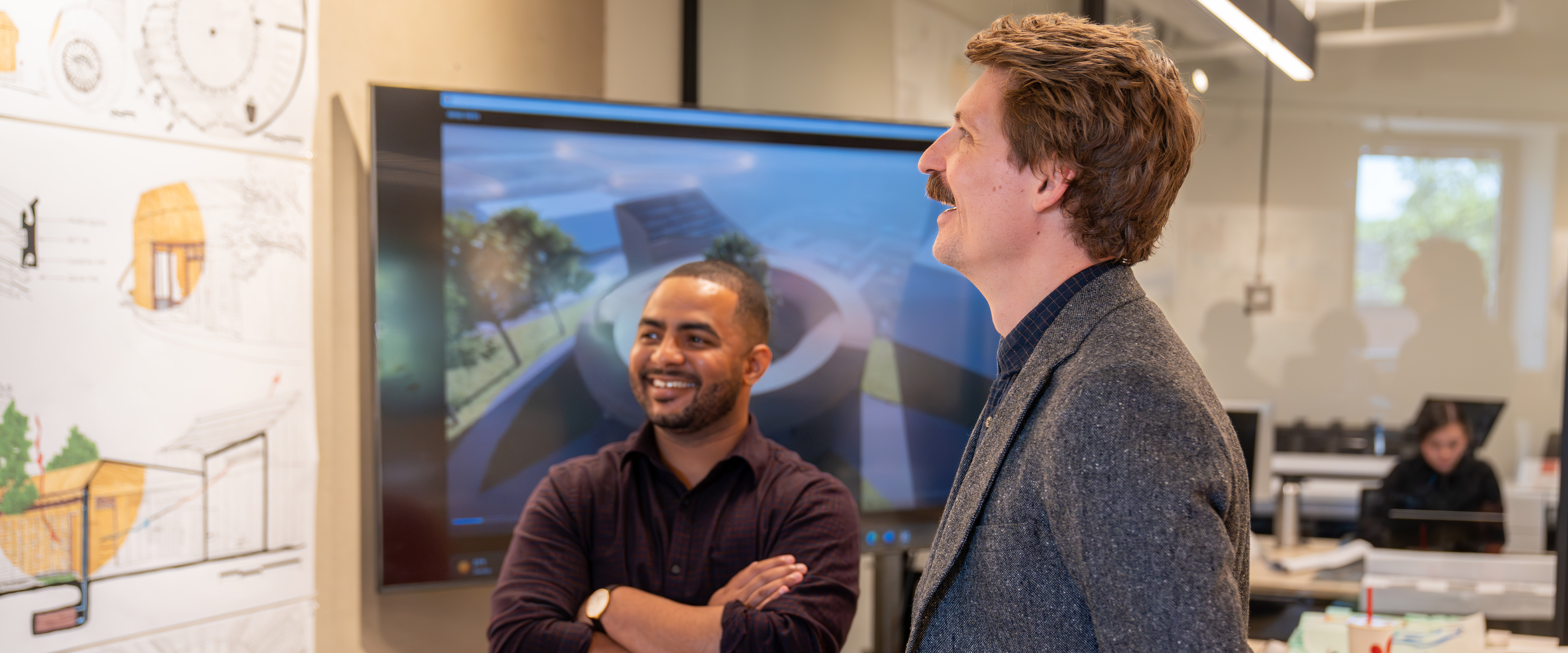 2 men looking at the architecture projects on the wall