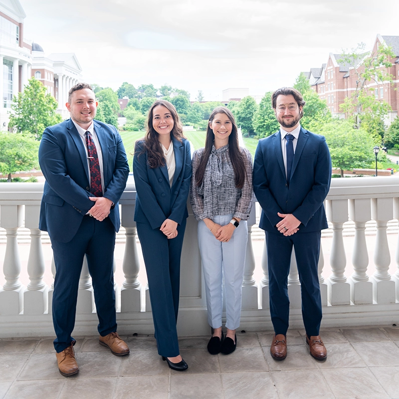 Four fellows pose for a photo together outside in front of a columned porch.