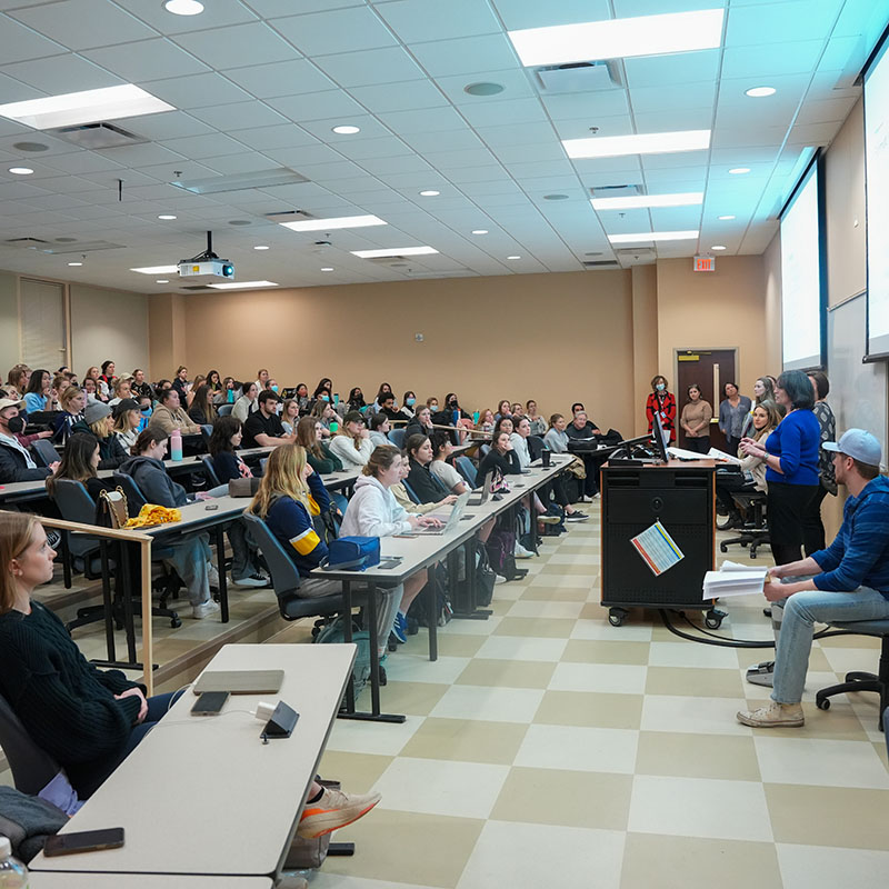 Classroom full for students listening to a panel of professors lecture