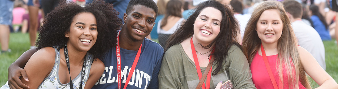 Four students sitting together and smiling while sitting on Belmont's lawn