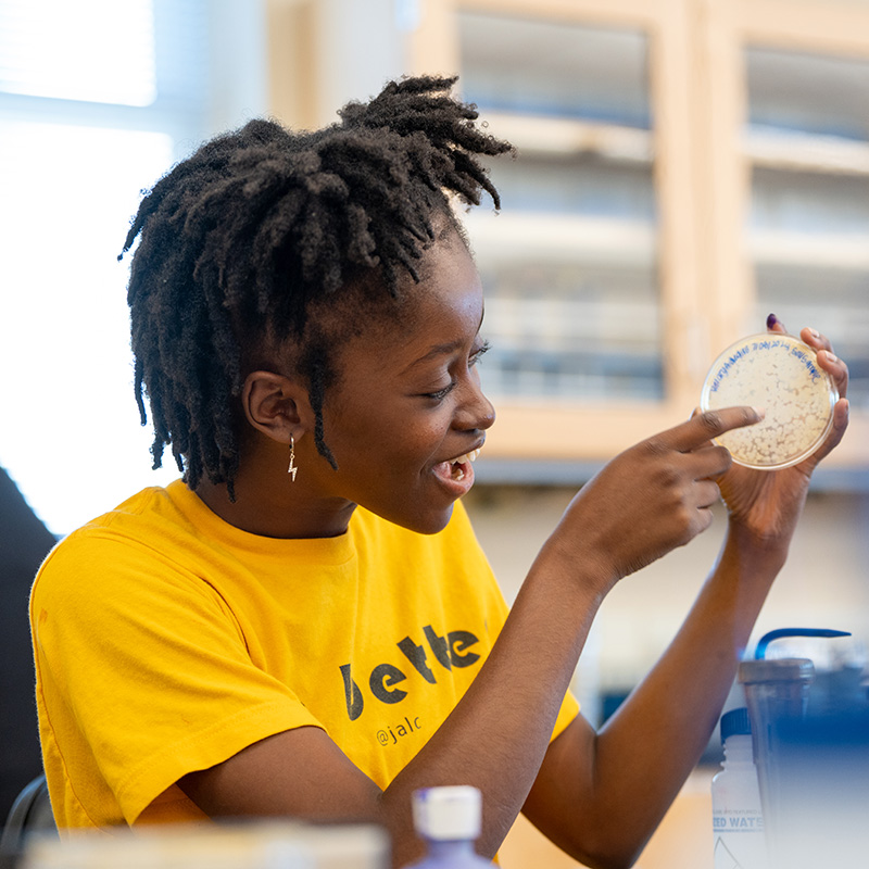 Student holding up and pointing to petri dish 