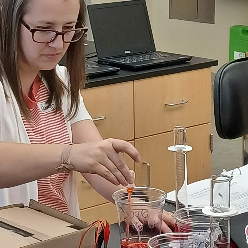 A teacher measuring a solution into a chemisty glass.