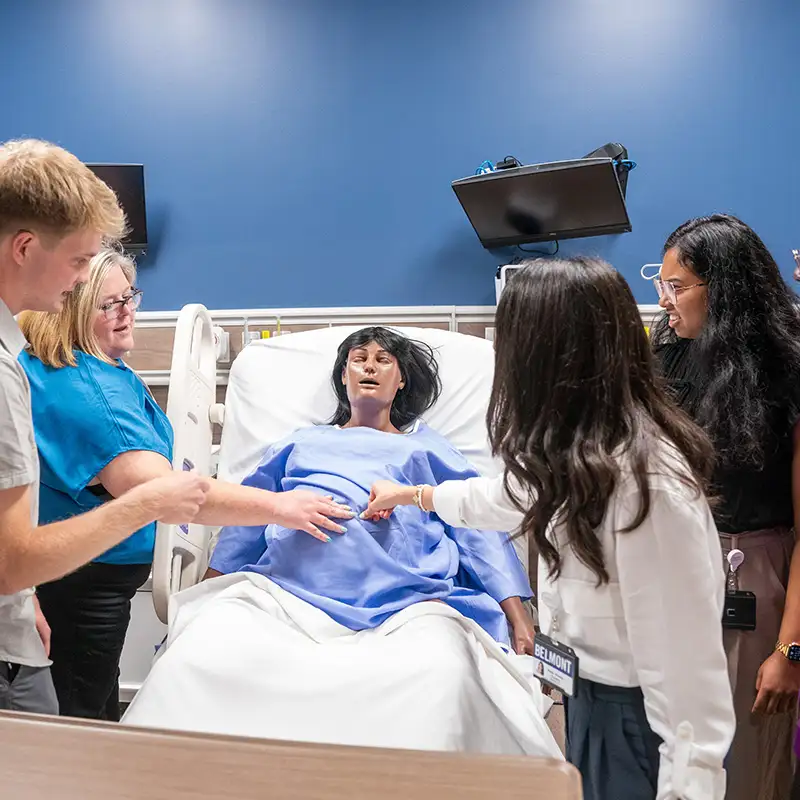 Students gathered around medical mannequin in a hospital bed