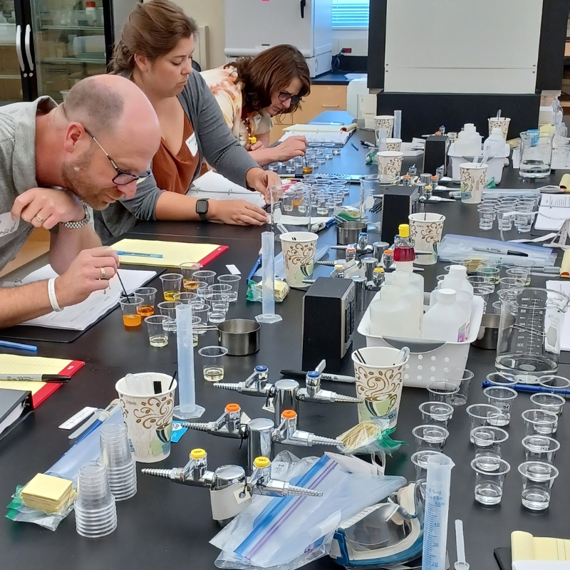 Adult Educators in a lab leaning over petri dishes and lab equipment