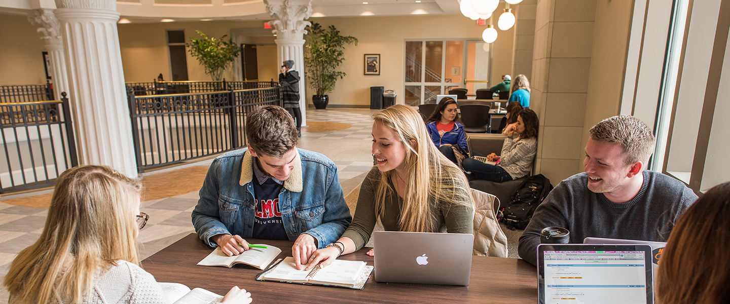 Students in an educational building with columns studying with their laptops.