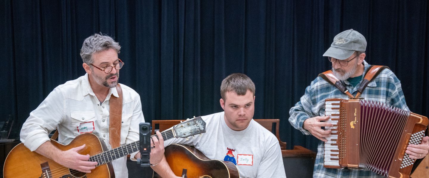 Three singers, two with a guitar and one with an accordion, perform a song they wrote