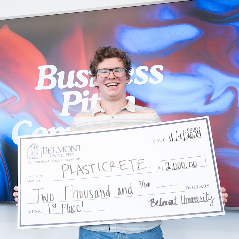 male student holding a giant check worth $2000 made out to his company Plasticrete