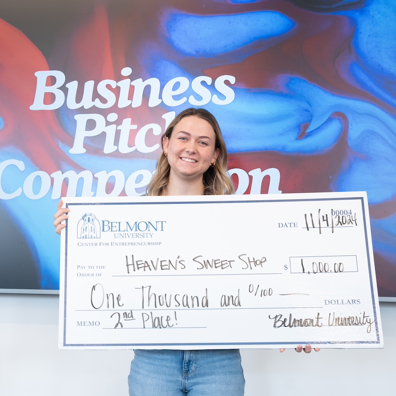 female student holding a giant check worth $1000 made out to her company Heaven's Sweet Shop