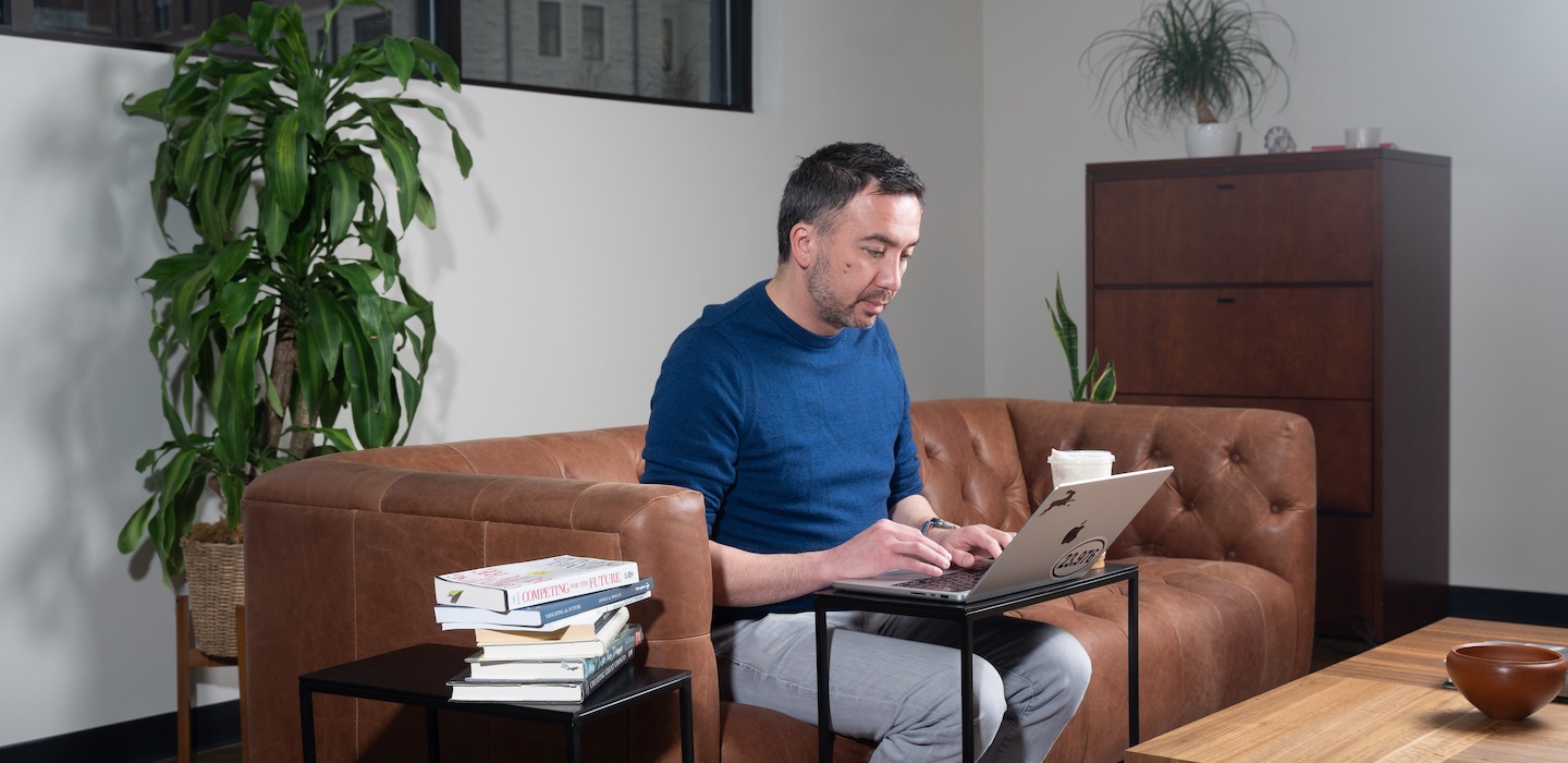 man uses laptop on couch in a business setting