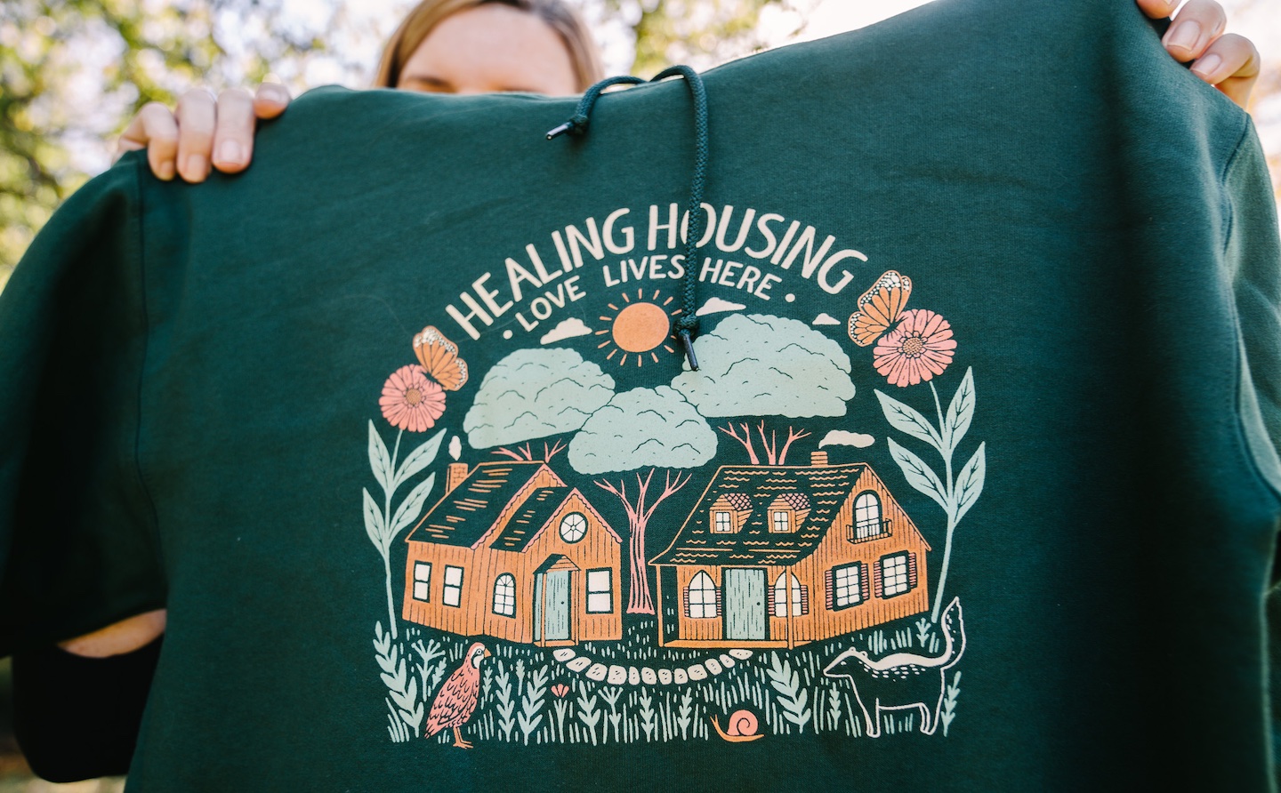 Amy Hodges Hamilton holds up a green sweatshirt that reads healing house