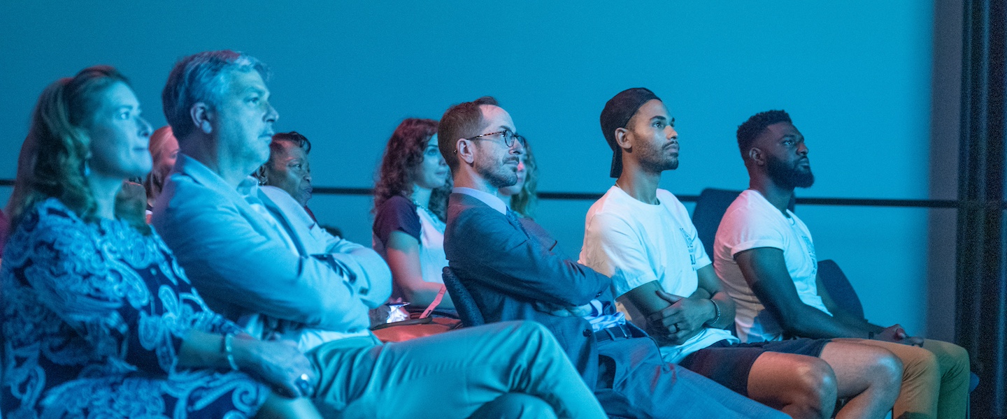 five seated people watching a film being shown off-camera