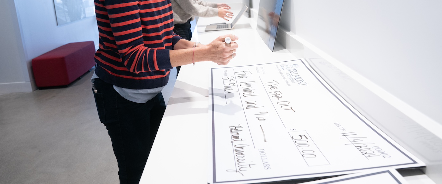 woman filling out giant check to company "The Far Out" for $500