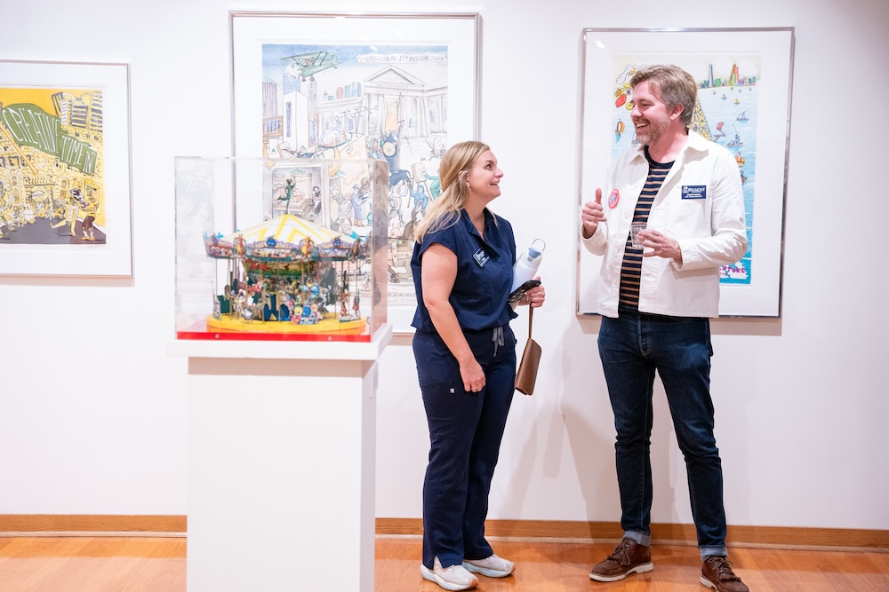 two visitors chat in front of Red Grooms artwork on the wall