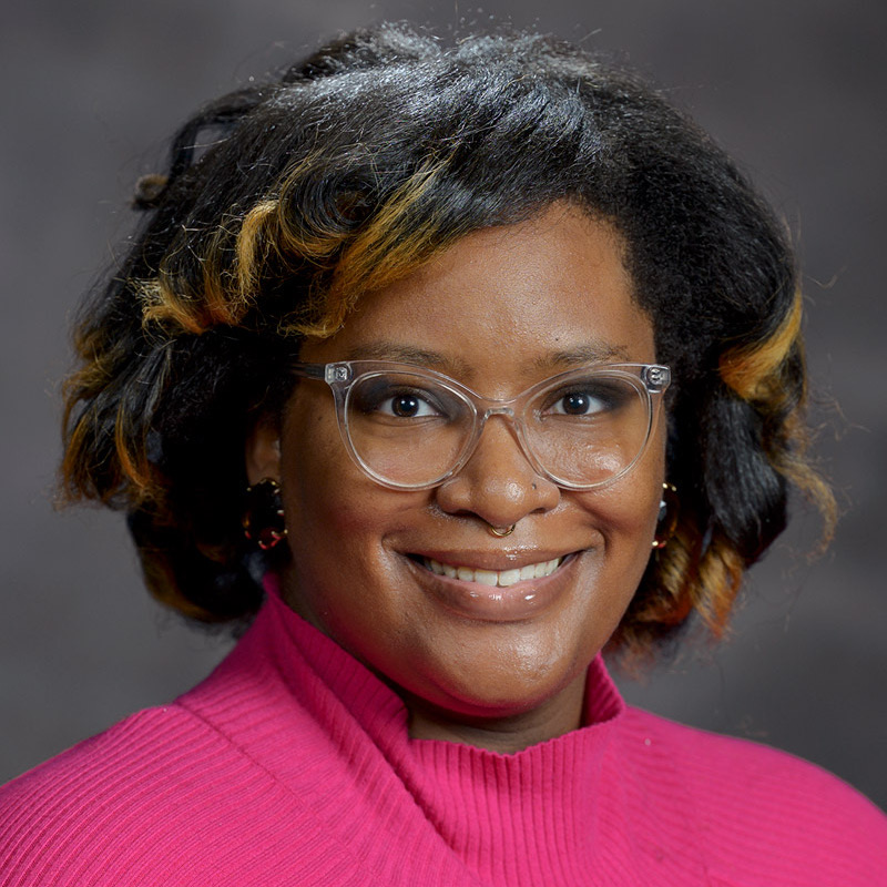 Nia Allen's headshot, wearing a bright pink shirt and clear glasses