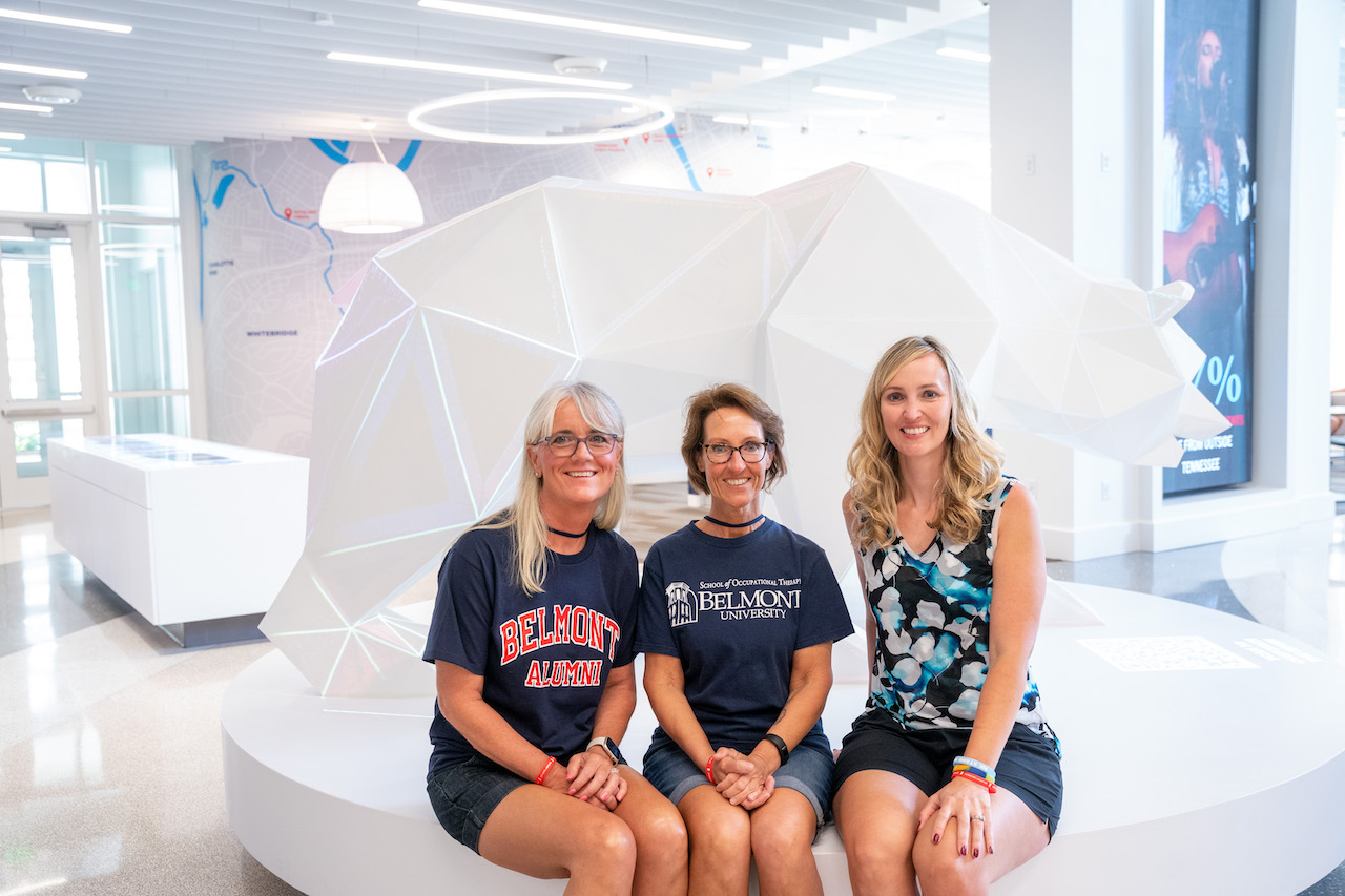 Three alumna pose for picture in front of bear statue