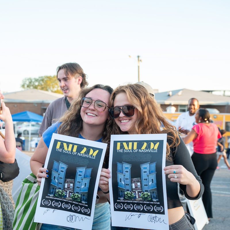 two girls smiling holding up posters for "Exit 207"